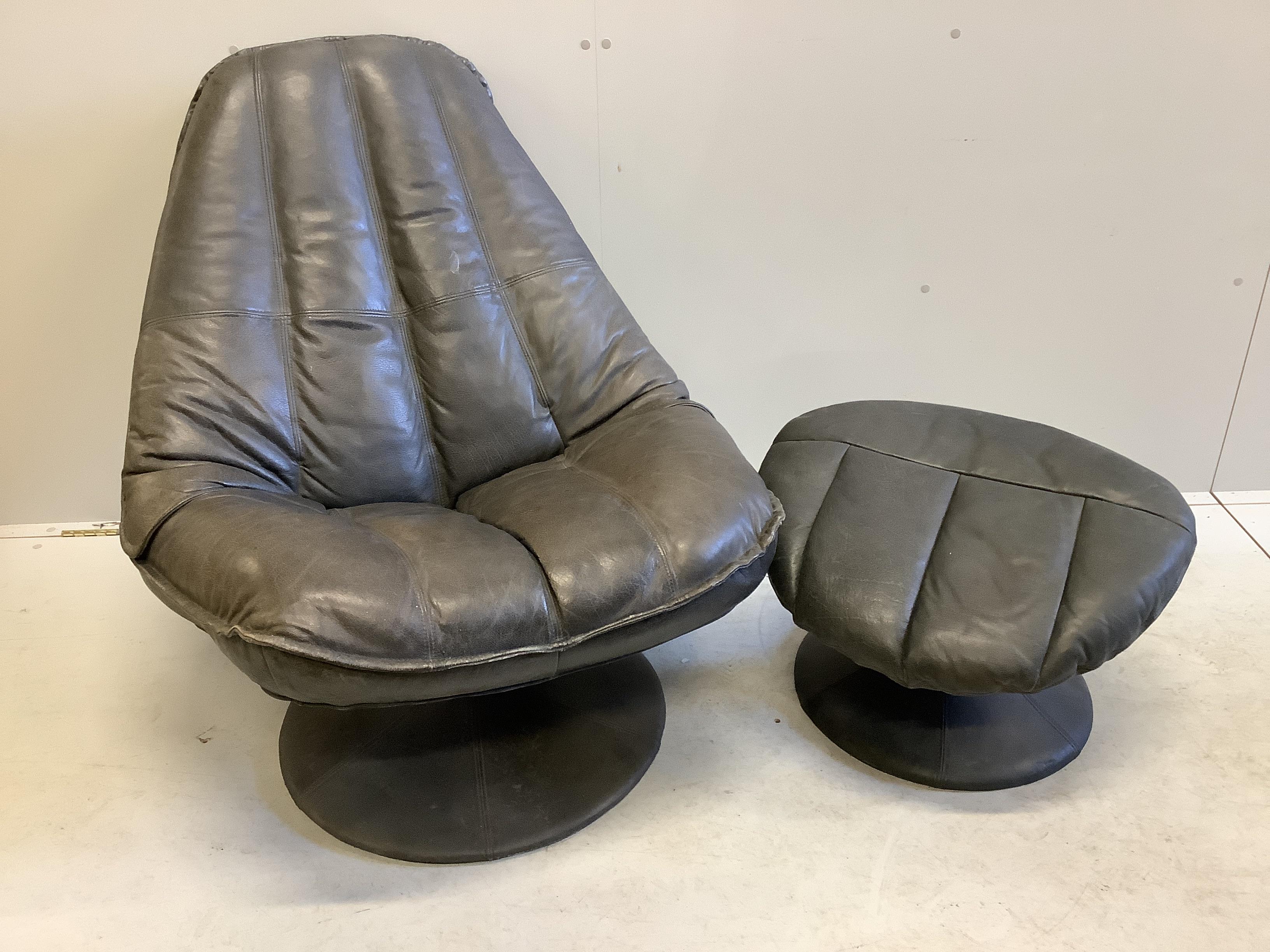 A mid century black leather revolving armchair, width 82cm, height 95cm and footstool